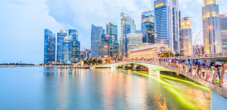 Panorama nowoczesnego miasta z wieżowcami nad wodą i oświetlonym mostem pełnym przechodniów o zmierzchu