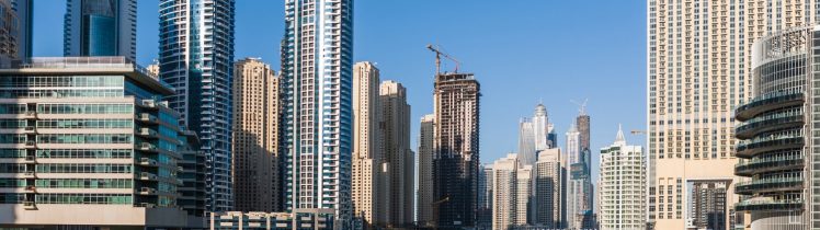 Nowoczesne wieżowce nad kanałem w Dubaju w słoneczny dzień, z mariną, łodziami i trwającą budową jednego z budynków.