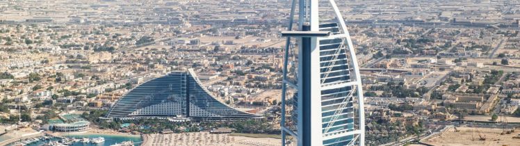 Widok z lotu ptaka na Burj Al Arab w Dubaju, luksusowy hotel na sztucznej wyspie, turkusowe morze, plażę i nowoczesną zabudowę miasta w tle.