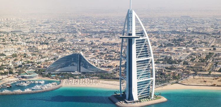 Widok z lotu ptaka na Burj Al Arab w Dubaju, luksusowy hotel na sztucznej wyspie, turkusowe morze, plażę i nowoczesną zabudowę miasta w tle.