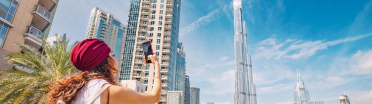 Turystka robiąca zdjęcie panoramy Dubaju z widokiem na Burj Khalifa, nowoczesne wieżowce i palmy w centrum miasta.