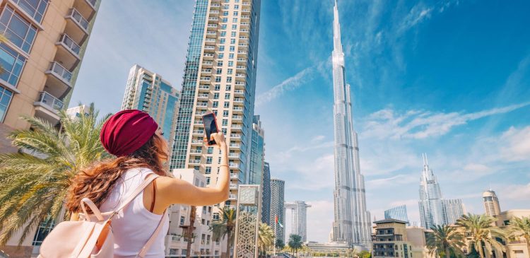 Turystka robiąca zdjęcie panoramy Dubaju z widokiem na Burj Khalifa, nowoczesne wieżowce i palmy w centrum miasta.