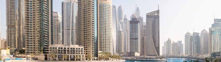 Dubai Marina z turkusową wodą kanału, nowoczesnymi apartamentowcami Emaar i promenadą z palmami w słoneczny dzień.