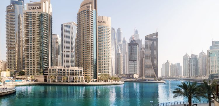 Dubai Marina z turkusową wodą kanału, nowoczesnymi apartamentowcami Emaar i promenadą z palmami w słoneczny dzień.