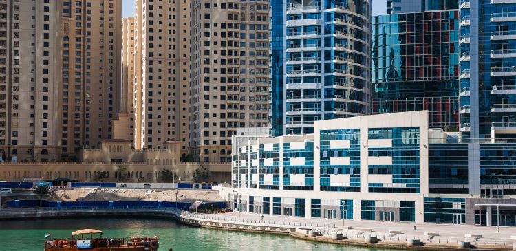 Dubai Marina z turkusowym kanałem, tradycyjną łodzią abra i nowoczesnymi apartamentowcami w tle.