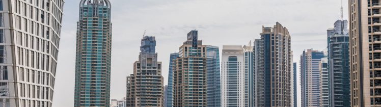 Dubai Marina z widokiem na nowoczesne wieżowce mieszkalne, luksusowe jachty w marinie oraz nadmorską promenadę otoczoną palmami.