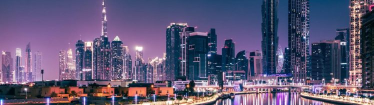 Nocna panorama Dubaju z oświetlonymi wieżowcami i odbiciem świateł w wodzie, z widocznym Burj Khalifa w tle