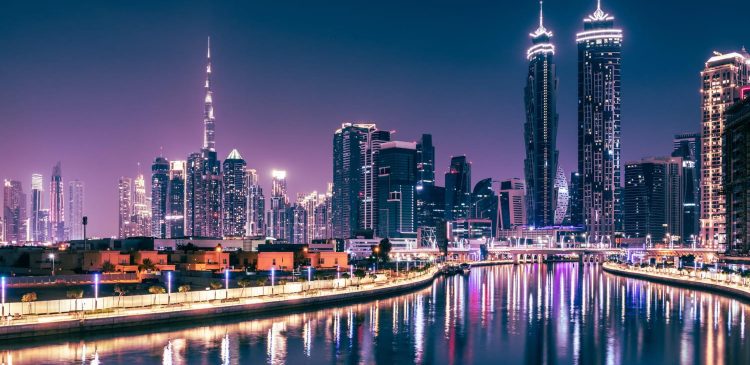 Nocna panorama Dubaju z oświetlonymi wieżowcami i odbiciem świateł w wodzie, z widocznym Burj Khalifa w tle