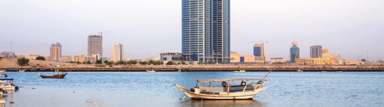 Nadbrzeże w Ras Al Khaimah z łodziami rybackimi na spokojnej wodzie i nowoczesnym wieżowcem w tle.
