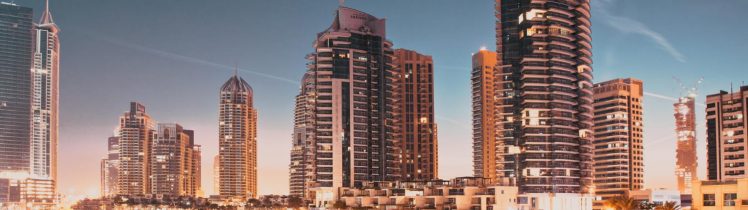 Nocna panorama Dubai Marina z oświetlonymi wieżowcami odbijającymi się w wodzie kanału i luksusową zabudową nadbrzeżną