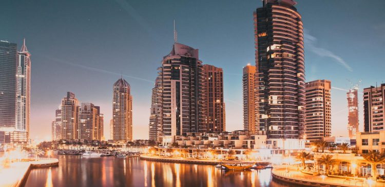 Nocna panorama Dubai Marina z oświetlonymi wieżowcami odbijającymi się w wodzie kanału i luksusową zabudową nadbrzeżną