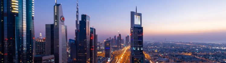 Nocna panorama Dubaju z Sheikh Zayed Road, oświetlone wieżowce i ruch samochodowy tworzący świetlne smugi w centrum miasta.