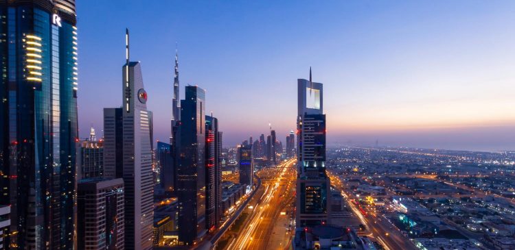 Nocna panorama Dubaju z Sheikh Zayed Road, oświetlone wieżowce i ruch samochodowy tworzący świetlne smugi w centrum miasta.