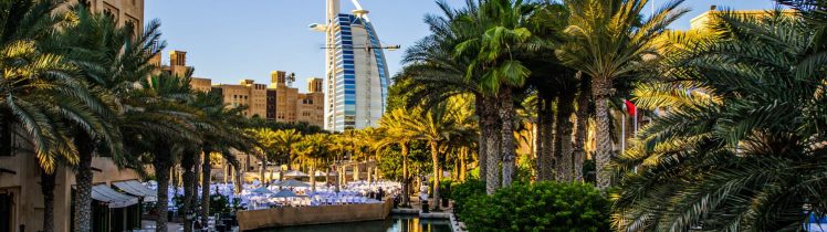 Widok na Madinat Jumeirah z kanałem wodnym, palmami i hotelem Burj Al Arab w tle w słoneczny dzień