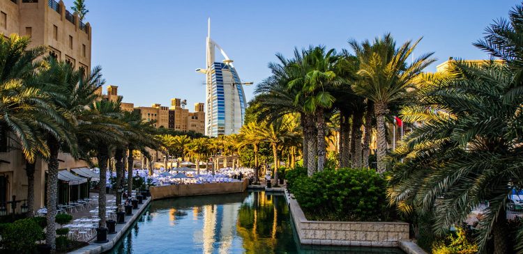 Widok na Madinat Jumeirah z kanałem wodnym, palmami i hotelem Burj Al Arab w tle w słoneczny dzień
