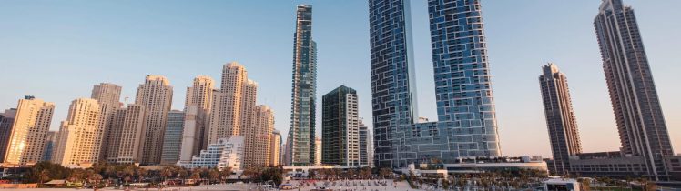 Panorama Dubaju z plażą i nowoczesnymi wieżowcami nad Zatoką Perską o zachodzie słońca