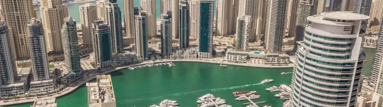 Widok z góry na Dubai Marina z turkusową wodą, mariną pełną jachtów oraz nowoczesnymi wieżowcami i diabelskim młynem Ain Dubai w tle