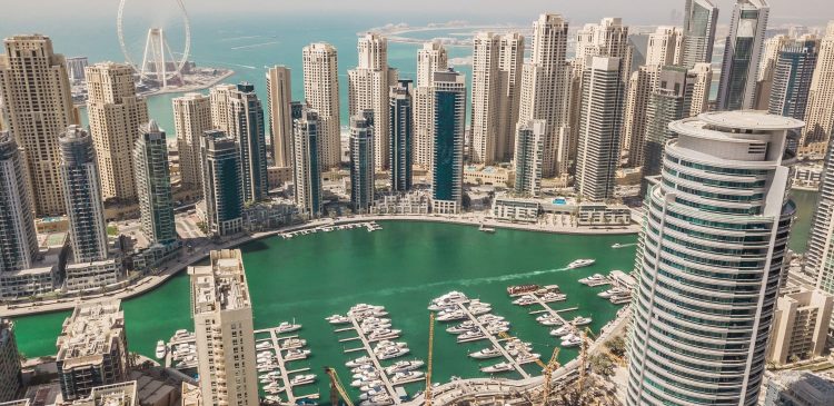 Widok z góry na Dubai Marina z turkusową wodą, mariną pełną jachtów oraz nowoczesnymi wieżowcami i diabelskim młynem Ain Dubai w tle