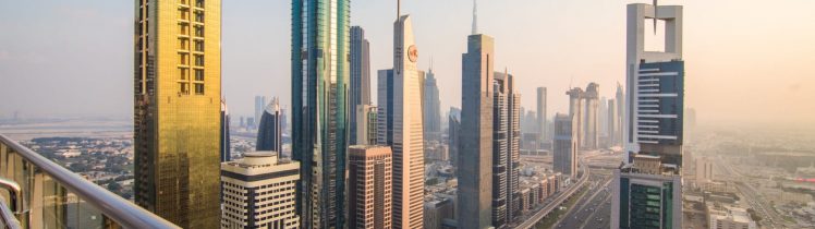 Widok na panoramę Dubaju z wysokości – nowoczesne wieżowce przy Sheikh Zayed Road oraz stacja metra, ujęcie z balkonu w świetle zachodzącego słońca