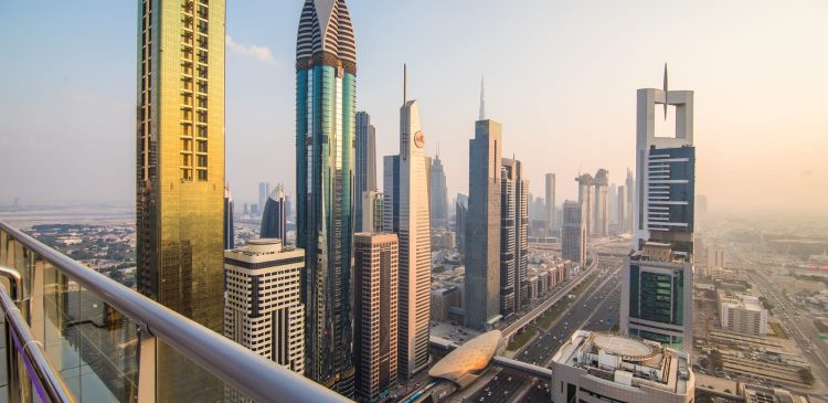 Widok na panoramę Dubaju z wysokości – nowoczesne wieżowce przy Sheikh Zayed Road oraz stacja metra, ujęcie z balkonu w świetle zachodzącego słońca