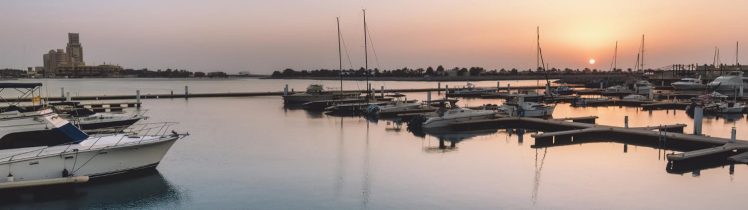 Marina na wyspie Marjan w Ras Al Khaimah o zachodzie słońca, spokojna woda z zacumowanymi jachtami i widokiem na linię brzegową