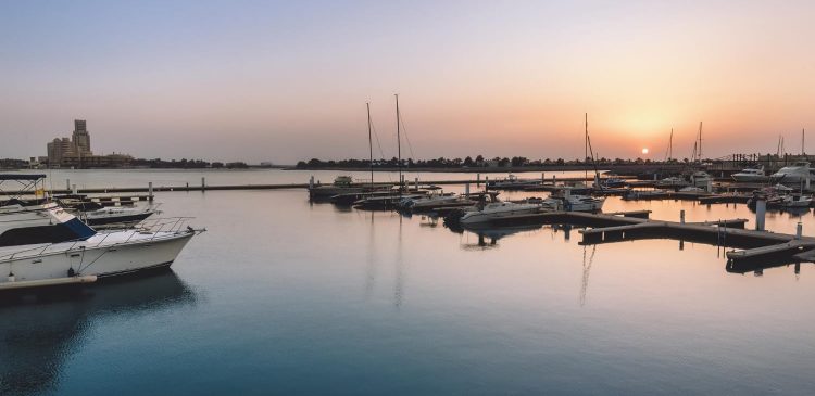 Marina na wyspie Marjan w Ras Al Khaimah o zachodzie słońca, spokojna woda z zacumowanymi jachtami i widokiem na linię brzegową