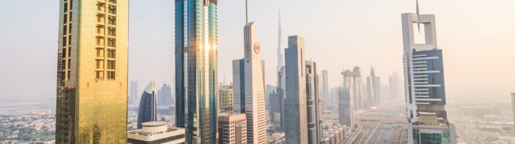 Panorama nowoczesnego centrum Dubaju z wieżowcami przy Sheikh Zayed Road i widokiem na Burj Khalifa o zachodzie słońca.