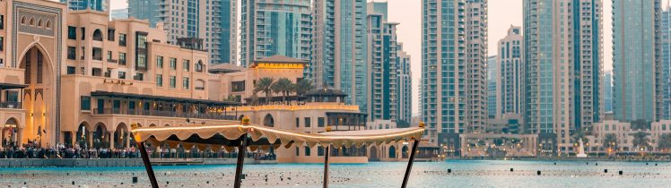 Tradycyjna łódź abra na wodach Dubai Downtown z widokiem na nowoczesne wieżowce i zabudowę w tle.