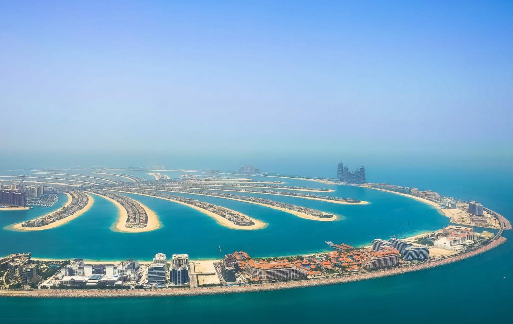 Widok z lotu ptaka na Palm Jumeirah w Dubaju z turkusową wodą, luksusowymi apartamentami i sztuczną wyspą w kształcie palmy.