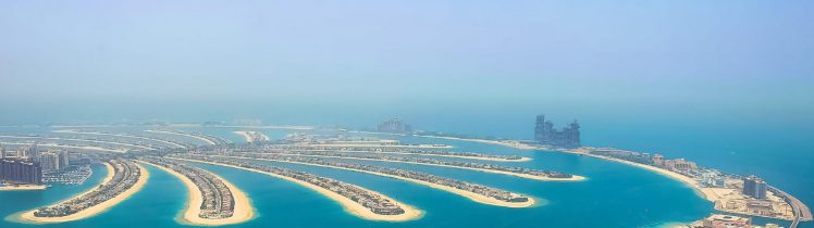 Widok z lotu ptaka na Palm Jumeirah w Dubaju z turkusową wodą, luksusowymi apartamentami i sztuczną wyspą w kształcie palmy.