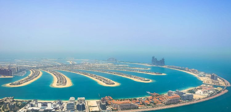 Widok z lotu ptaka na Palm Jumeirah w Dubaju z turkusową wodą, luksusowymi apartamentami i sztuczną wyspą w kształcie palmy.